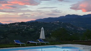 A swimming pool with lounge chairs and an umbrella, surrounded by a mountainous landscape. - Villa Collebelvedere - Apartment West - Home Restaurant (Fara Sabina (RI))