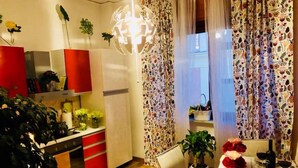 Una cocina moderna con armarios rojos, una encimera blanca y una lámpara colgante. Hay una zona de comedor con una mesa preparada para dos personas, una silla y una planta en maceta.