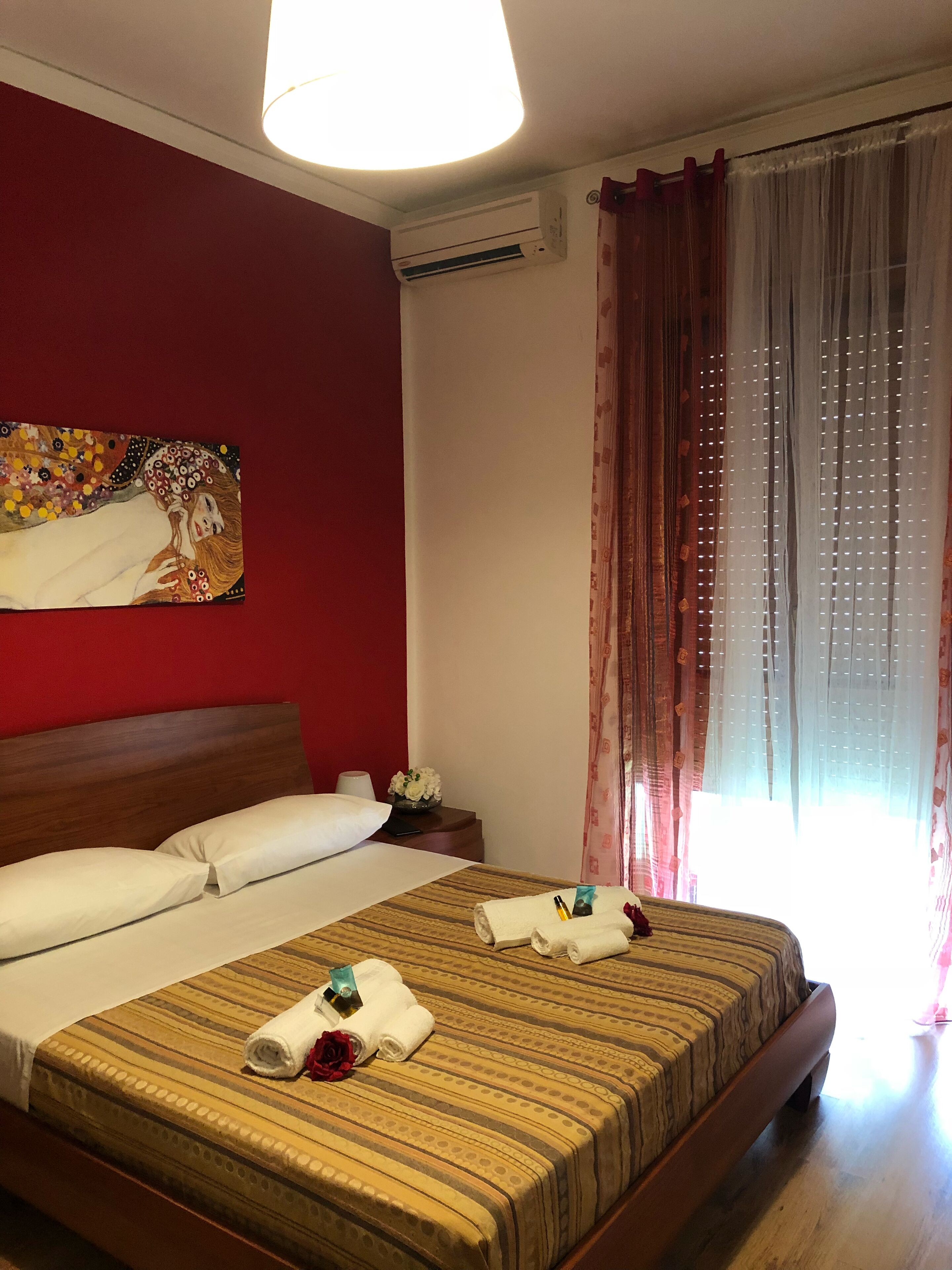 Quarto de hotel com uma cama grande, mesa de cabeceira, abajur, quadro na parede e janela com cortinas.