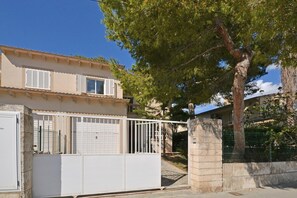 A two-story house with a gated entrance, a stone pillar, and a tree in the background.