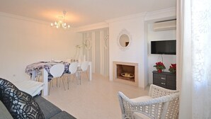 Una sala de estar con sofá, mesa de comedor, sillas, chimenea y televisor montado en la pared.
