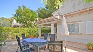 Un patio al aire libre con una mesa para dos, sillas alrededor y una pérgola arriba.
