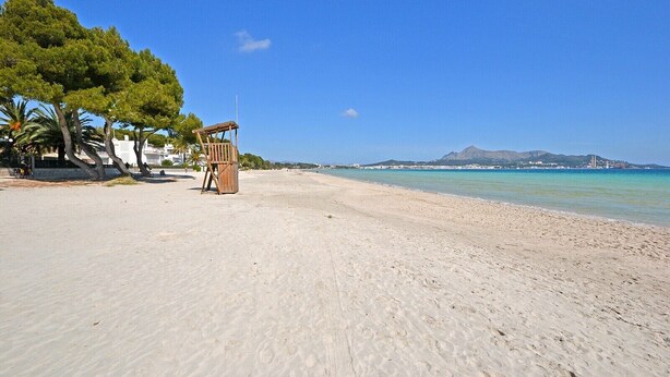 Una playa con una torre de salvavidas, palmeras y una montaña al fondo.