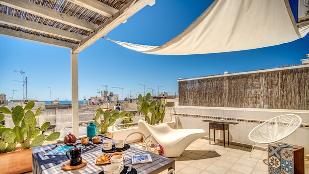 A rooftop terrace with a table set for a meal, surrounded by potted cacti and a white chair. - Il Nido - Le Case di Valentina (Gallipoli)