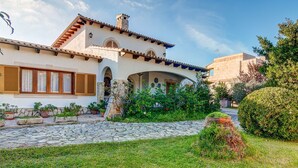 Una casa de estilo mediterráneo tradicional con un camino de piedra que conduce a la entrada, rodeada de jardines cuidados y un cielo azul despejado.