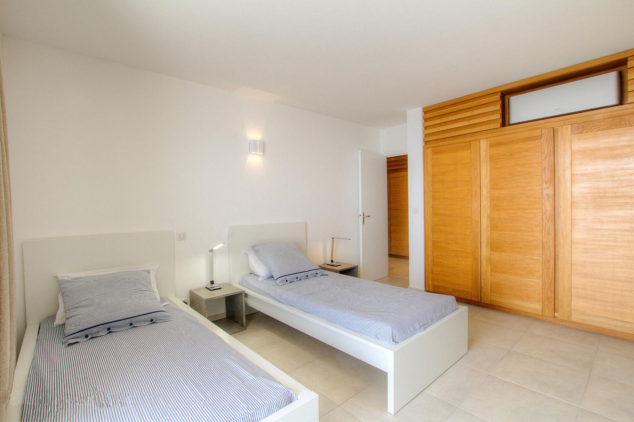 A bedroom with two single beds, a wooden wardrobe, and a bedside table with a lamp.