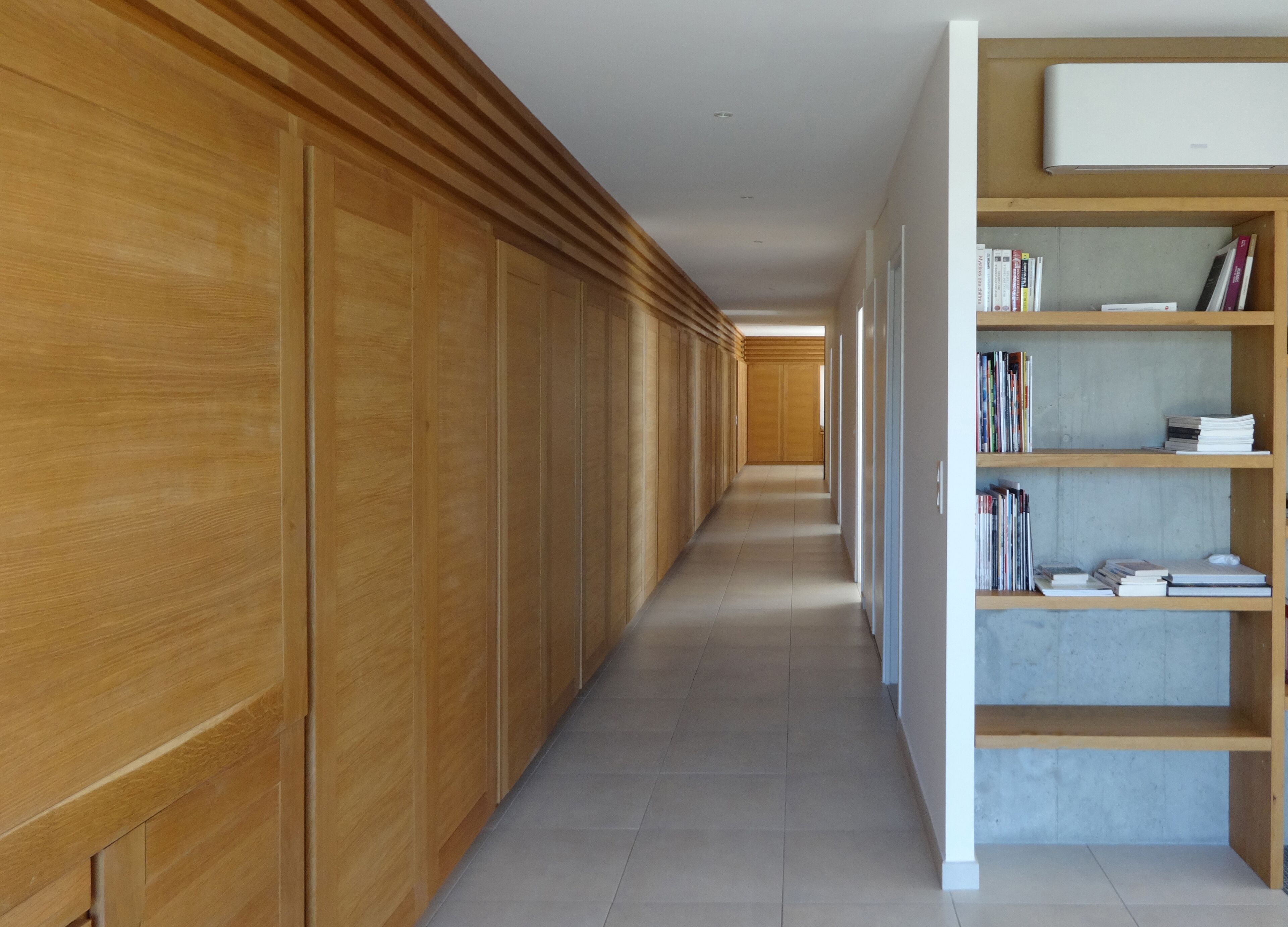 A long, narrow hallway with wooden paneling on one side and a bookshelf on the other.