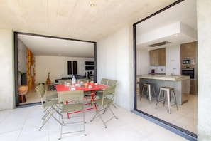 A modern kitchen with a central island, bar stools, and a dining area with a red table and green chairs. - VILLA ARCHITECTE 5☆ 180° SEA VIEW and TOUR GÉNOISE. HEATED POOL. INTIMACY. (Conca)