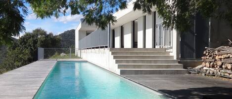 A modern pool area with a wooden deck, a concrete staircase, and a building with a white facade.