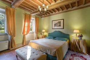 A bedroom with a bed, a bench, a chandelier, and a painting on the wall.