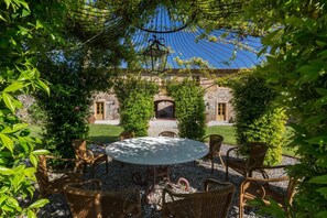 A round table with wicker chairs in a garden area with a stone building in the background.