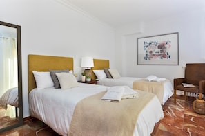 A hotel room with two beds, a nightstand with a lamp, a chair, and a painting on the wall.