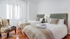 A hotel room with two beds, a chair, a table with a lamp, and a window with sheer curtains. - Genteel Home Gran Capitan Terrace (Granada)