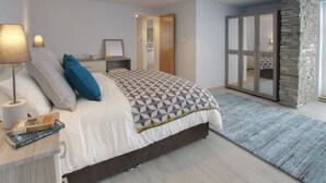 Une chambre à coucher comprenant un lit, des lampes de chevet, une table de chevet, un miroir, une commode, un mur d’accent en pierre et une vue sur la salle de bain.