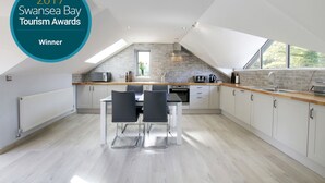 Une cuisine moderne avec un coin repas, dotée d’une verrière, de meubles blancs et d’un plan de travail en bois.