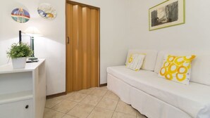 A room with a white sofa, a wooden door, a small table with a plant, and wall decorations. - Castellani Apartment (Firenze)