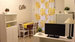 A small, compact room with a dining table, chairs, a TV, a lamp, and a shelf with a potted plant. - Castellani Apartment (Firenze)