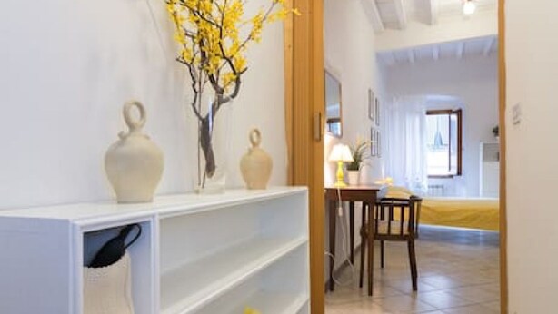 A hallway with white shelving units, a wooden door, and a dining area with a table and chairs. - Castellani Apartment (Firenze)
