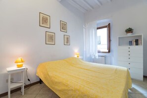 A bedroom with a bed, bedside lamps, a dresser, a window with curtains, and framed pictures on the wall. - Castellani Apartment (Firenze)