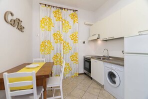 A compact kitchen with a dining area, a washing machine, and a curtain with a yellow pattern. - Castellani Apartment (Firenze)
