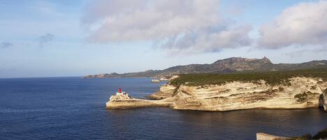 A coastal landscape with a lighthouse on a rocky outcrop, clear skies, and calm sea.