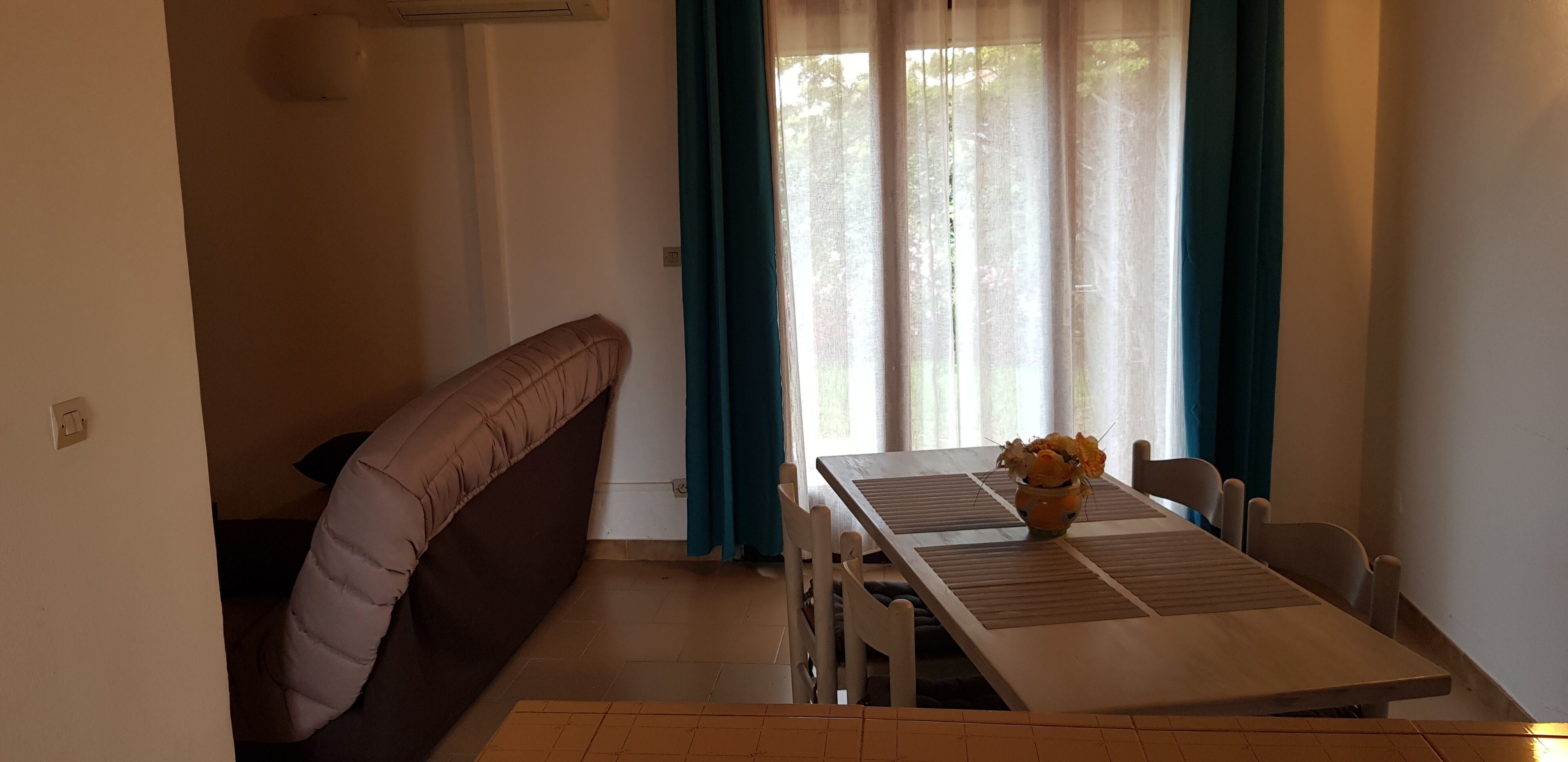 Un comedor con una mesa, sillas, un banco y una ventana con cortinas.