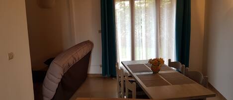 Un comedor con una mesa, sillas, un banco y una ventana con cortinas.