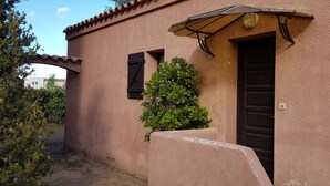 Un edificio con fachada de estuco color beige, una puerta negra y un ventanal con contraventanas.