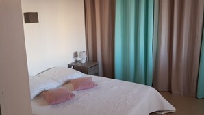 Una cama bien tendida con almohadas blancas y rosas, una mesita de noche con una lámpara y cortinas en tonos turquesa y beige.