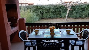 Un patio con una mesa lista para dos personas, rodeado por una valla de madera, y una vista de seto y árbol al fondo.