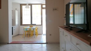 Una cocina con televisor, una mesa de comedor con sillas y un ventanal con cortinas.