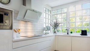 A modern kitchen with white cabinetry, a built-in oven, and a window with a view of greenery. - Genteel Home San Leandro (Sevilla)