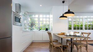 A modern kitchen with white cabinetry, a stainless steel refrigerator, a microwave, and a dining area with a wooden table and chairs. - Genteel Home San Leandro (Sevilla)