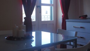 A dining area with a table and chairs, a window with curtains, and a cabinet with a television. - Ortigia, comfortable Baron house (Siracusa)