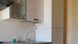 A modern kitchen with a white countertop, stainless steel sink, and a built-in oven. There is a green bottle of dish soap on the counter. - Ortigia, comfortable Baron house (Siracusa)