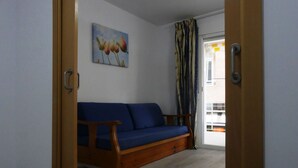A room with a wooden sofa, a painting on the wall, and a view through a door. - Alexis Plus Zeus Salou 4011 (Salou)
