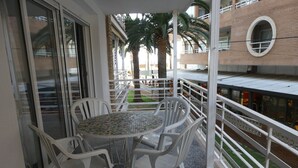 A balcony with a round table and white plastic chairs, overlooking a building with a brick facade and a circular window. - Alexis Plus Zeus Salou 4011 (Salou)