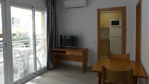 A compact room with a sliding glass door leading to an outdoor area, a small wooden desk with a television, a microwave, and a refrigerator. - Alexis Plus Zeus Salou 4011 (Salou)