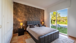A bedroom with a large bed, two bedside tables, and a view of a pool and garden through a sliding glass door. -  Beautiful sunny villa with pool and sea views Marbella (ELVIRIA) (Marbella)