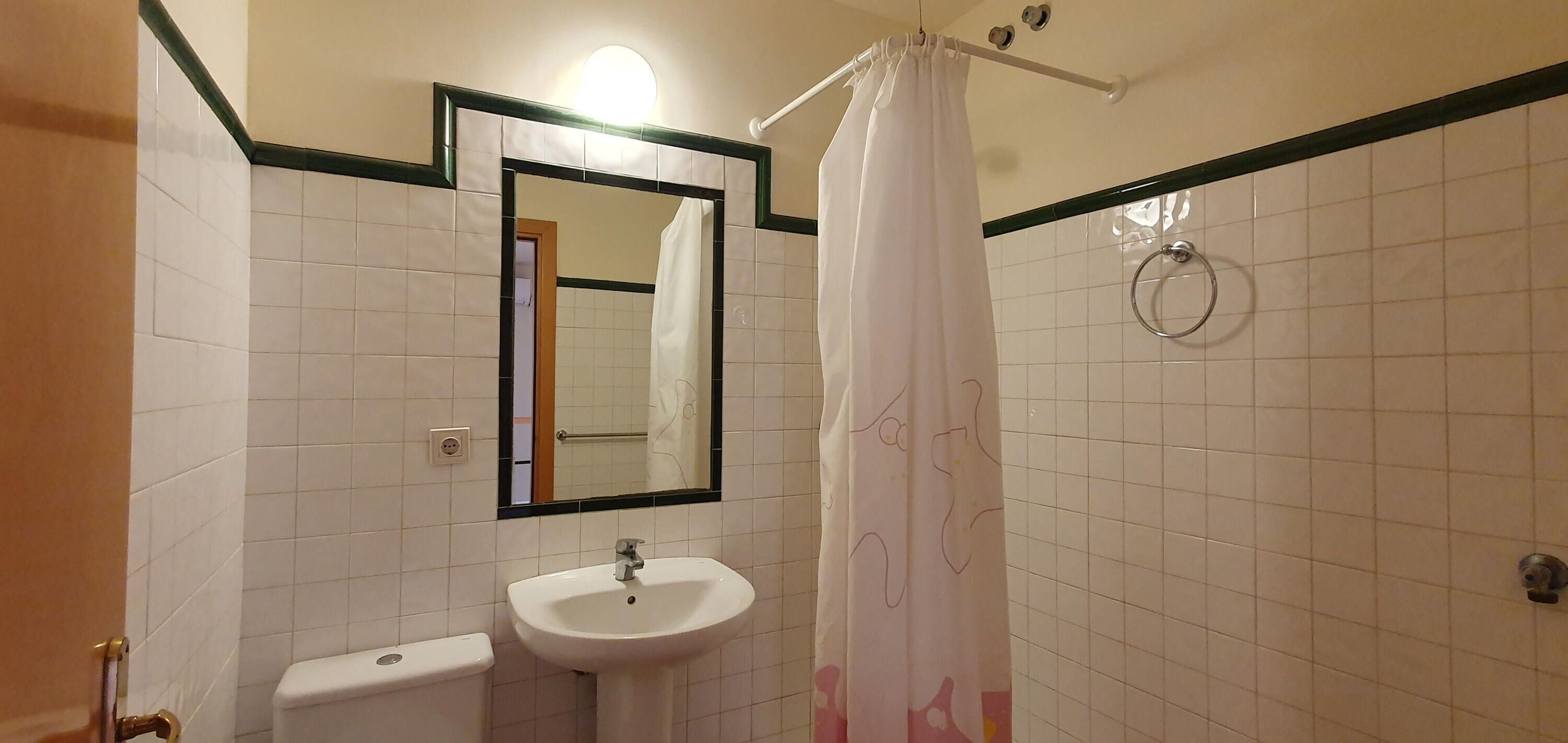 Un baño con lavamanos blanco, espejo y cortina de ducha.