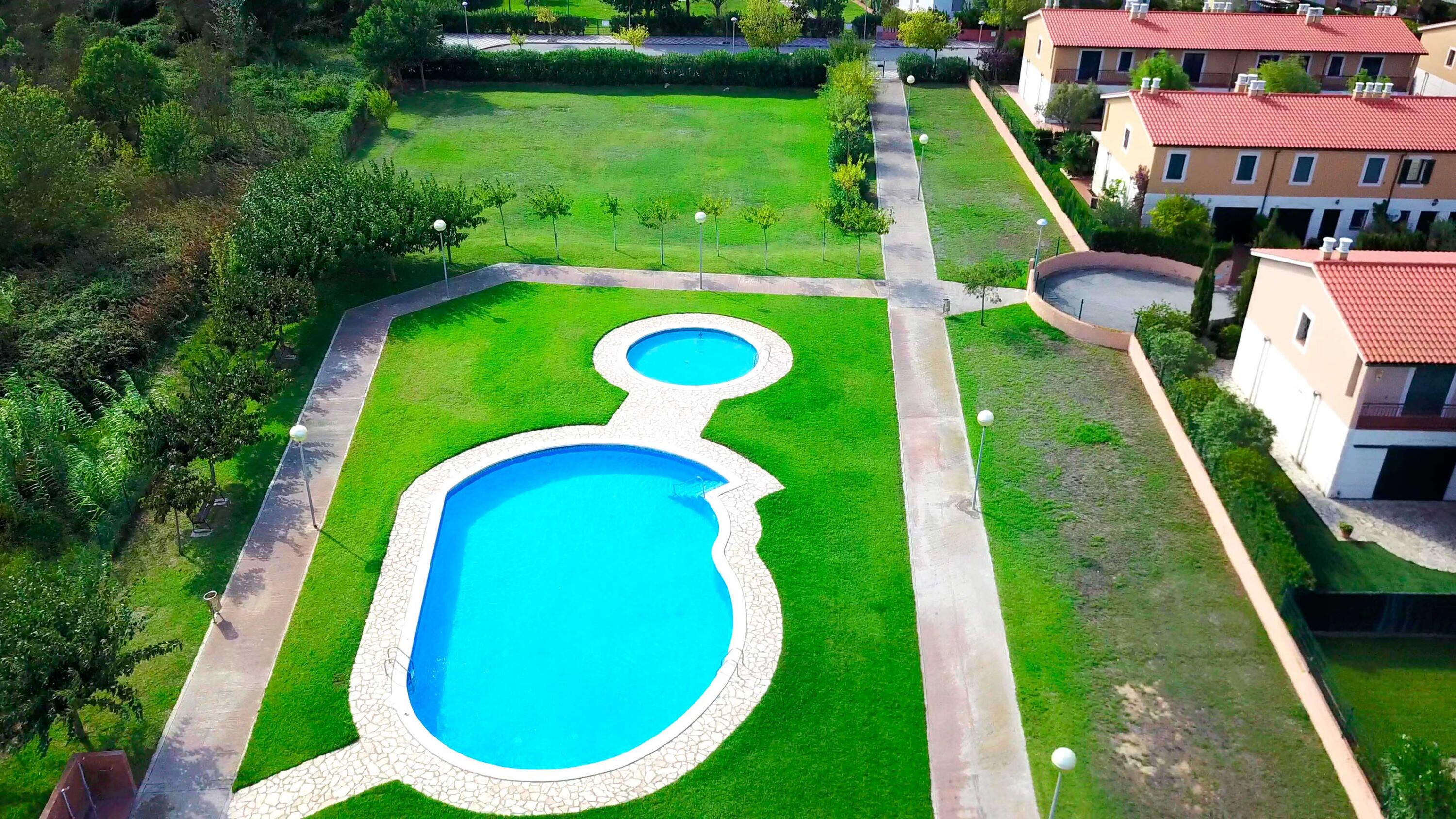 Una piscina de diseño único, rodeada de césped cuidado y un sendero pavimentado.