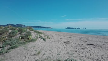 Una playa arenosa con vegetación escasa y formaciones rocosas a lo lejos.