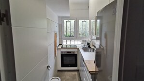 A narrow kitchen with white cabinets, a built-in oven, a sink, and a window providing natural light. - 20m2 porch, 1000m garden, barbecue, parking, fenced and protected and WIFI. (Rosas)