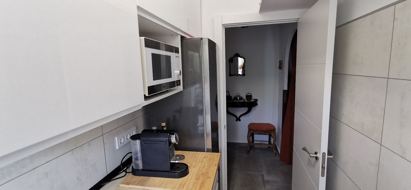 Una cocina compacta con microondas, cafetera y un pequeño taburete.