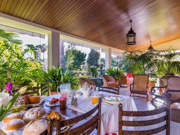 A covered outdoor dining area with wooden tables and chairs, surrounded by lush greenery and plants. - Can Mandol - Spectacular luxury house with pool and large garden (Inca)