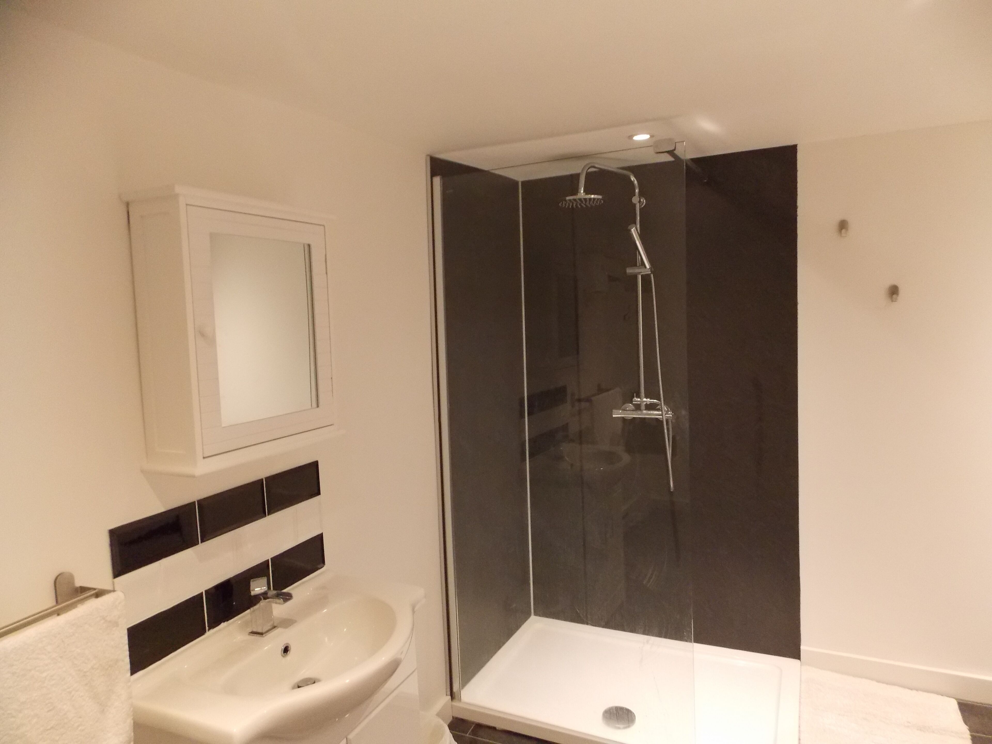 Ein modernes Badezimmer mit einer ein Glasfach raumseitig abgetrennten Dusche, einem weißen Waschbecken und einem Spiegel darüber.