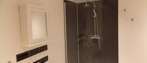 Ein modernes Badezimmer mit einer ein Glasfach raumseitig abgetrennten Dusche, einem weißen Waschbecken und einem Spiegel darüber.