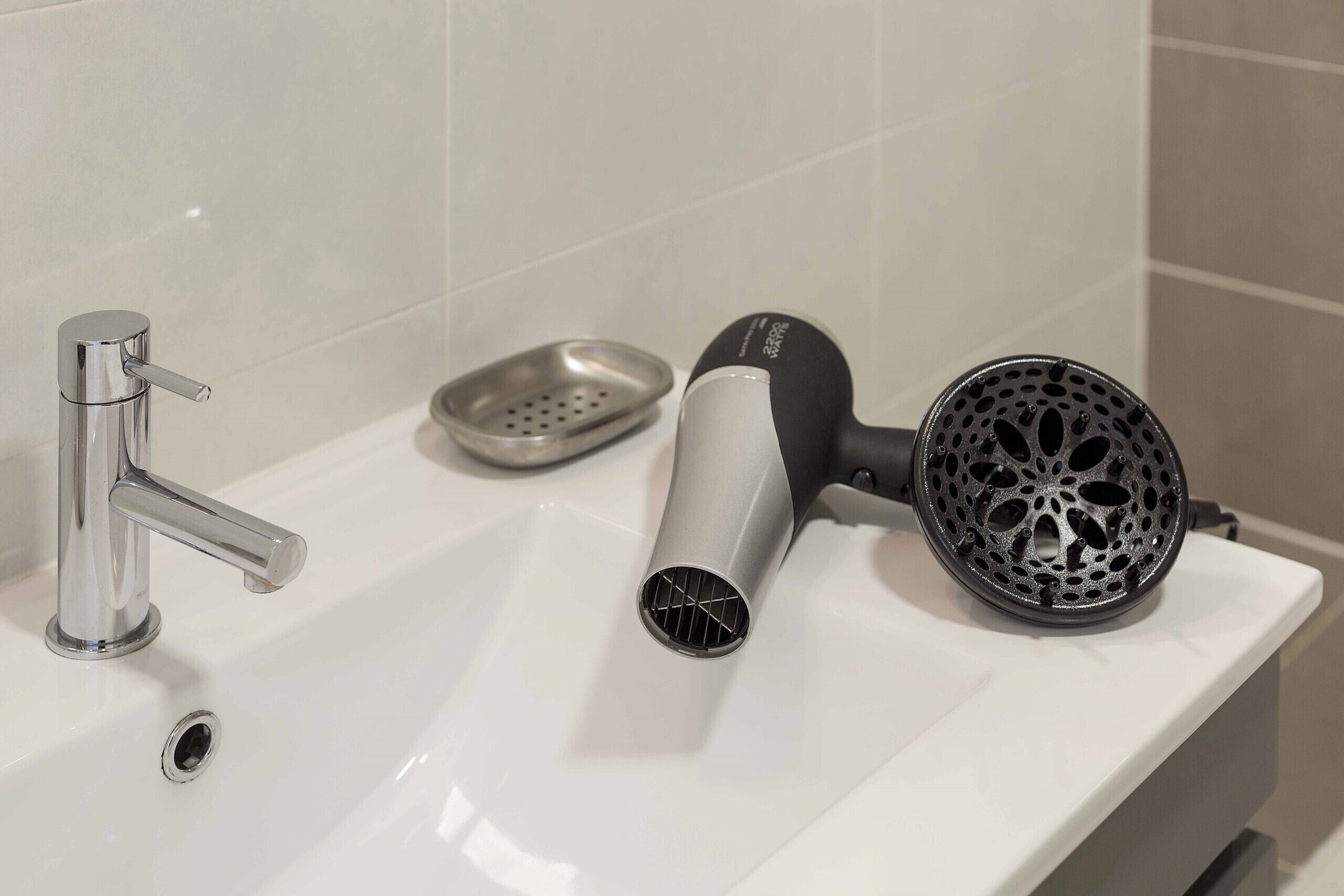Un lavabo de salle de bain avec un robinet chromé, un sèche-cheveux et un appareil noir pour coiffer les cheveux, le tout posé sur le comptoir.