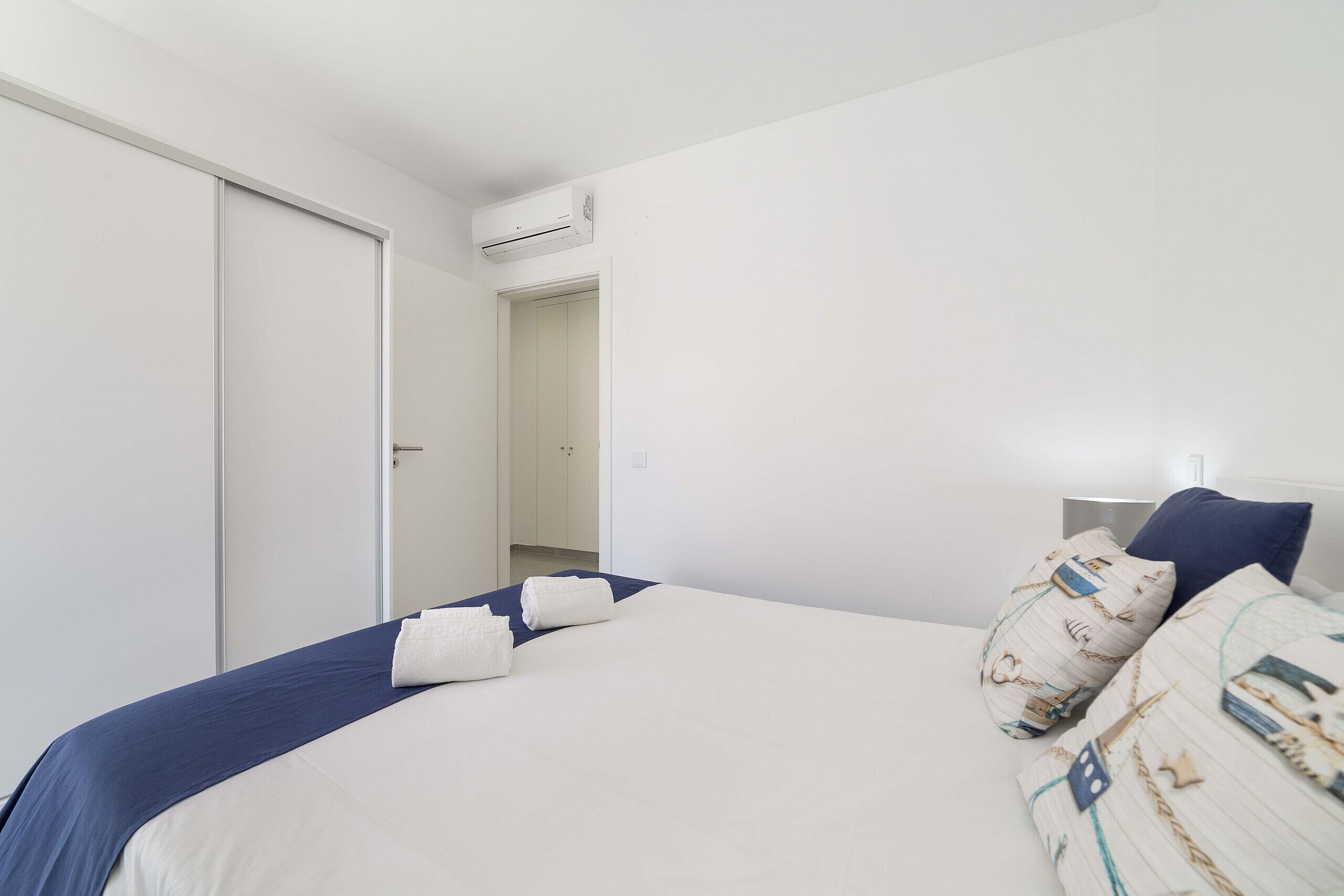 Quarto com cama, almofadas, mesa de cabeceira e ar condicionado.