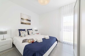 Quarto com cama, mesa de cabeceira, luminária, pintura e janela com cortinas.